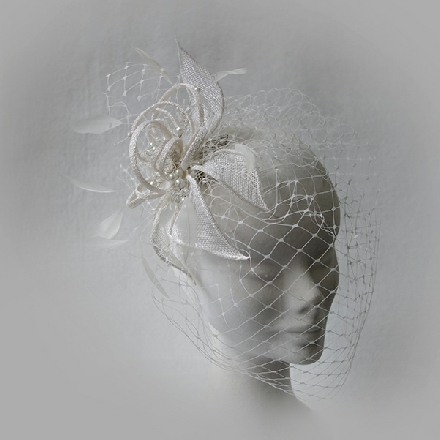 A feminine ivory flower fascinator with feathers, pearls and birdcage veil, perfect for brides.